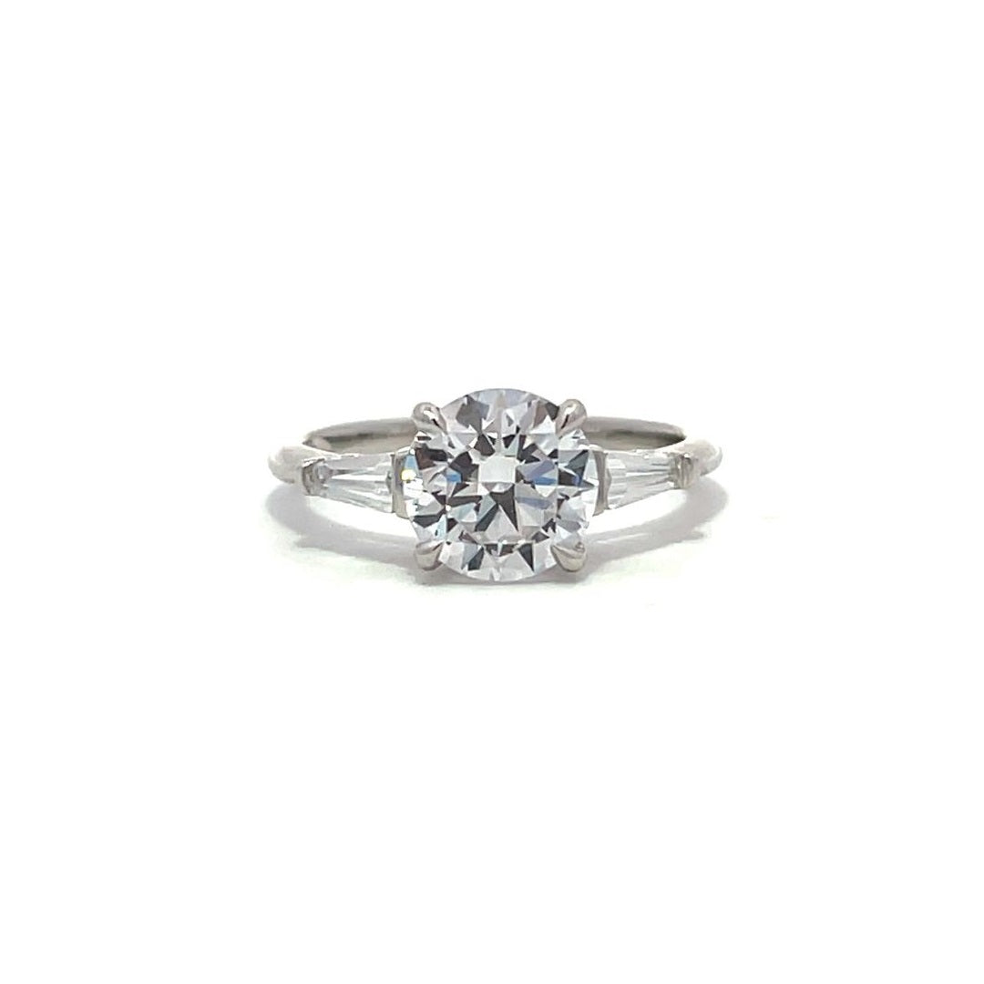 White gold three-stone diamond engagement ring with round-cut center stone and baguette side stones on a white background.