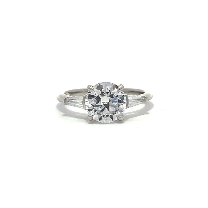  White gold three-stone diamond engagement ring with round-cut center stone and baguette side stones on a white background.