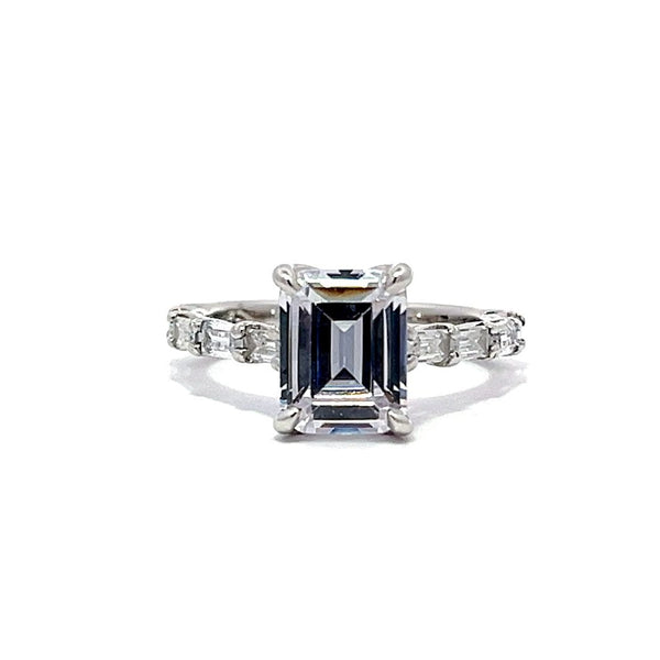 White gold emerald-cut diamond engagement ring with a diamond band on a white background.