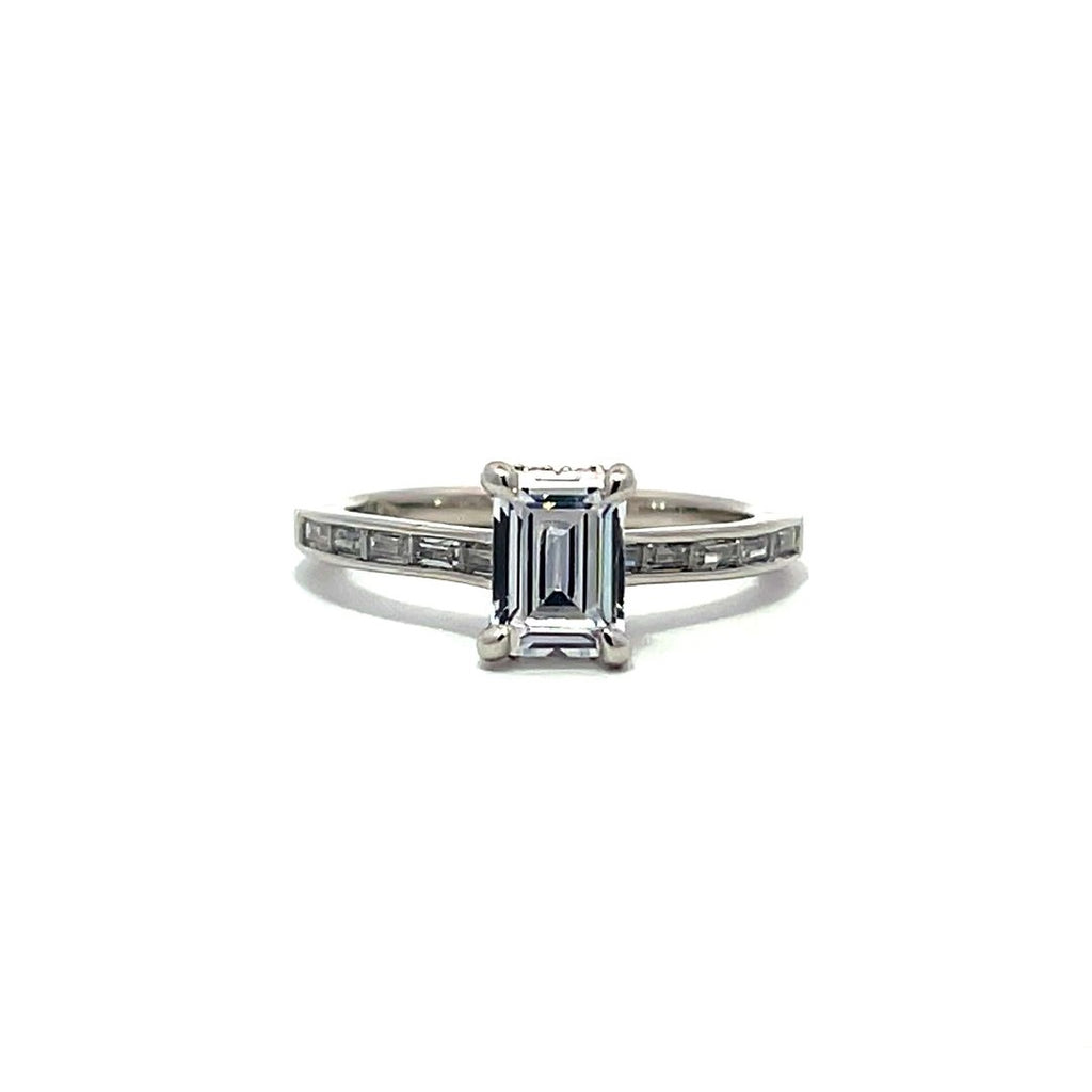 White gold emerald-cut diamond engagement ring with a diamond band on a white background.