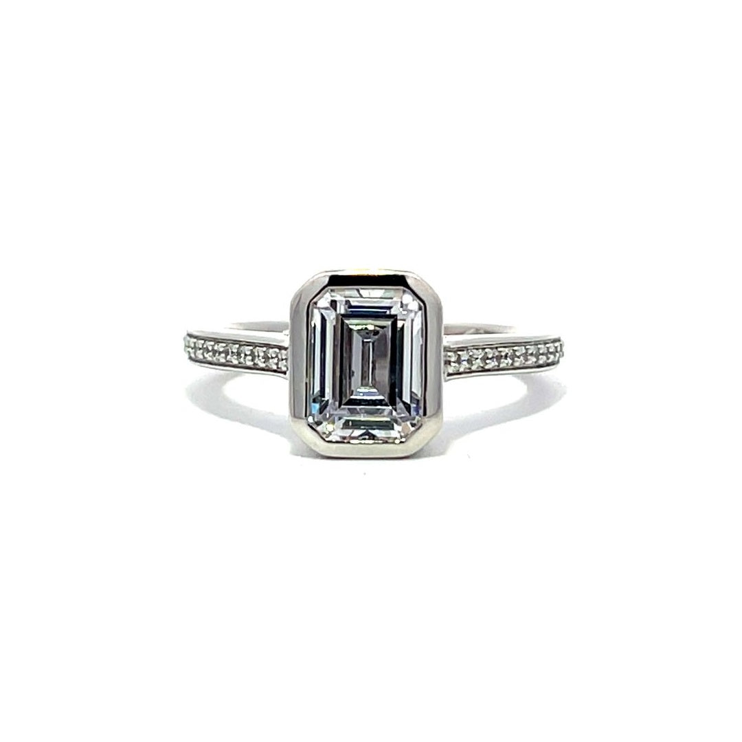 White gold emerald-cut diamond engagement ring with a diamond band on a white background.