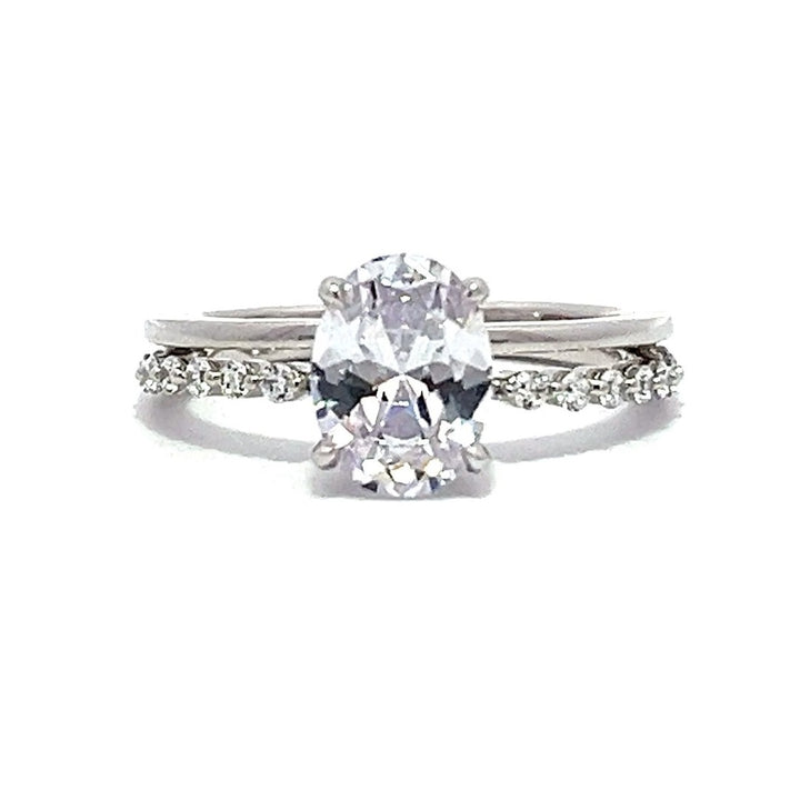 White gold oval-shaped diamond engagement ring with a diamond band on a white background.