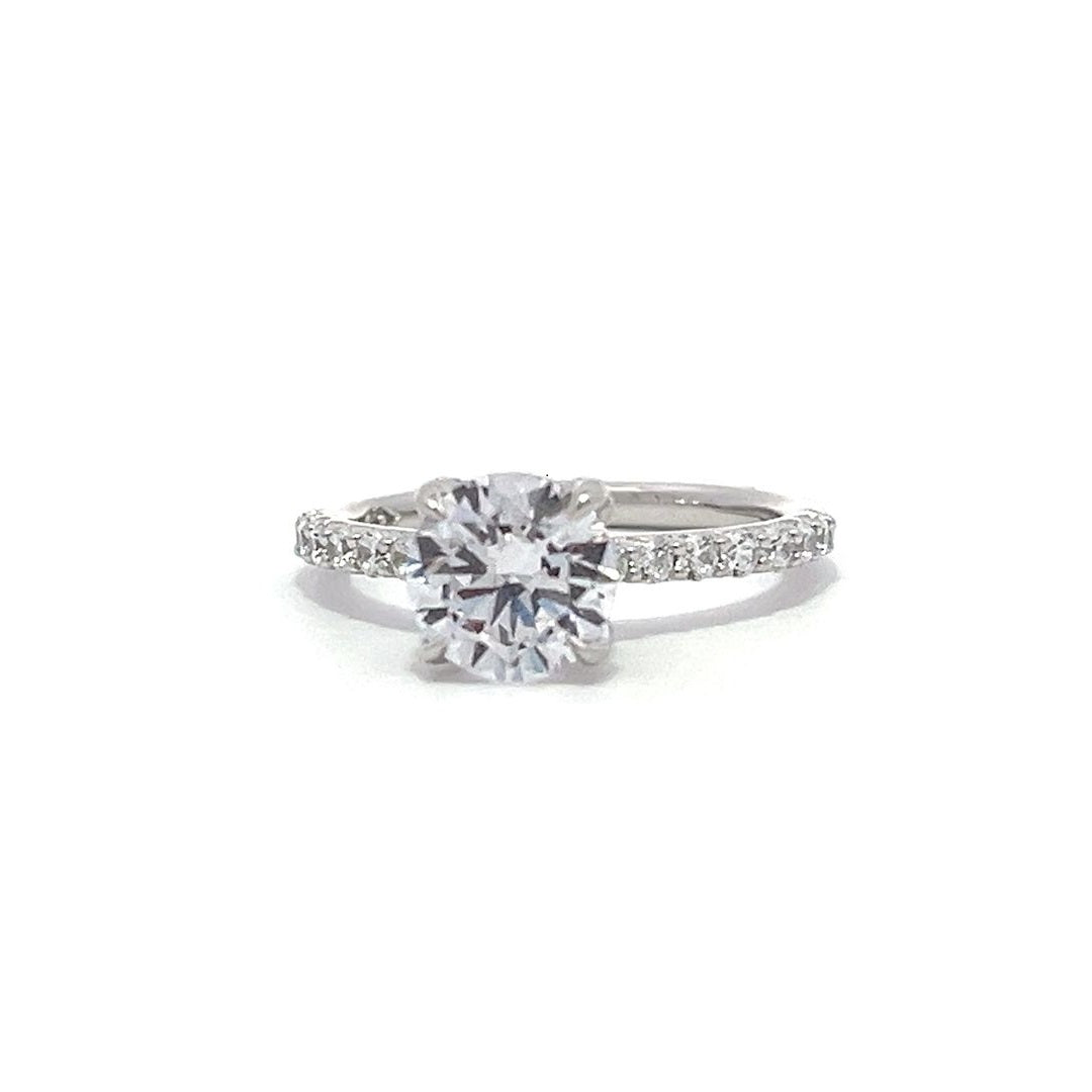 White gold round-shaped diamond engagement ring with a diamond band on a white background.