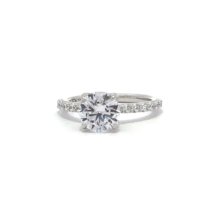 White gold round-shaped diamond engagement ring with a diamond band on a white background.