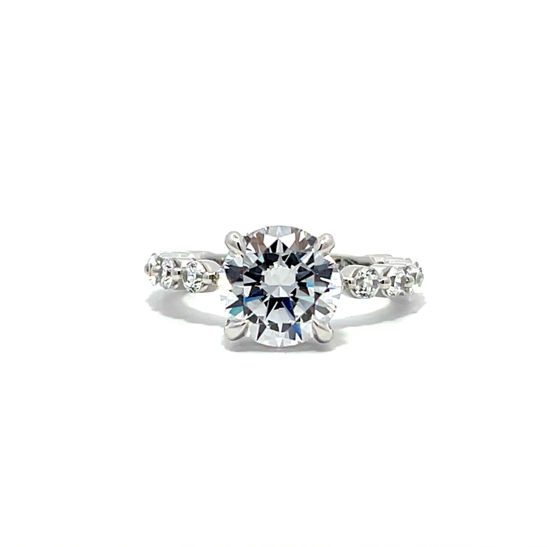 White gold round-shaped diamond engagement ring with a diamond band on a white background.