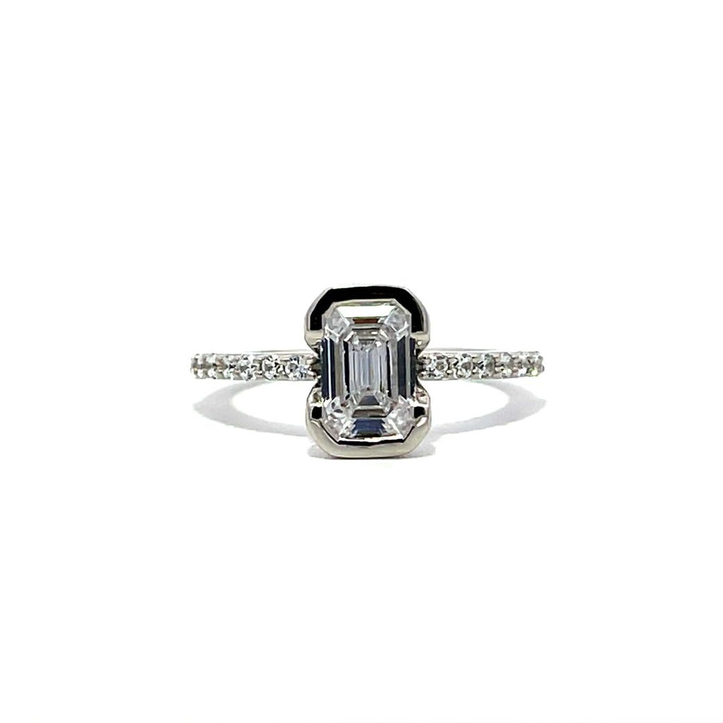 White gold emerald-cut diamond engagement ring with a diamond band on a white background.