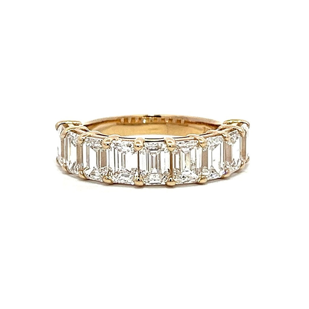 Yellow gold eternity band with emerald-cut diamonds on a white background.