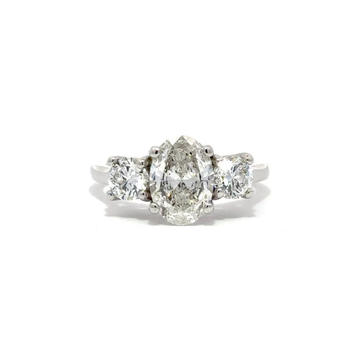 Silver three-stone engagement ring with pear-shaped center diamond and round side diamonds, on a white background.