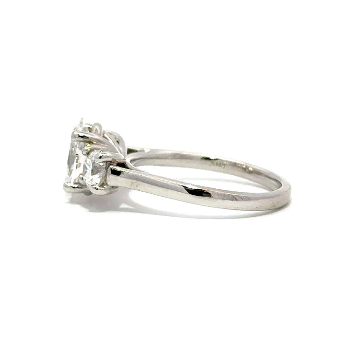 Silver three-stone engagement ring with pear-shaped center diamond and round side diamonds, on a white background.