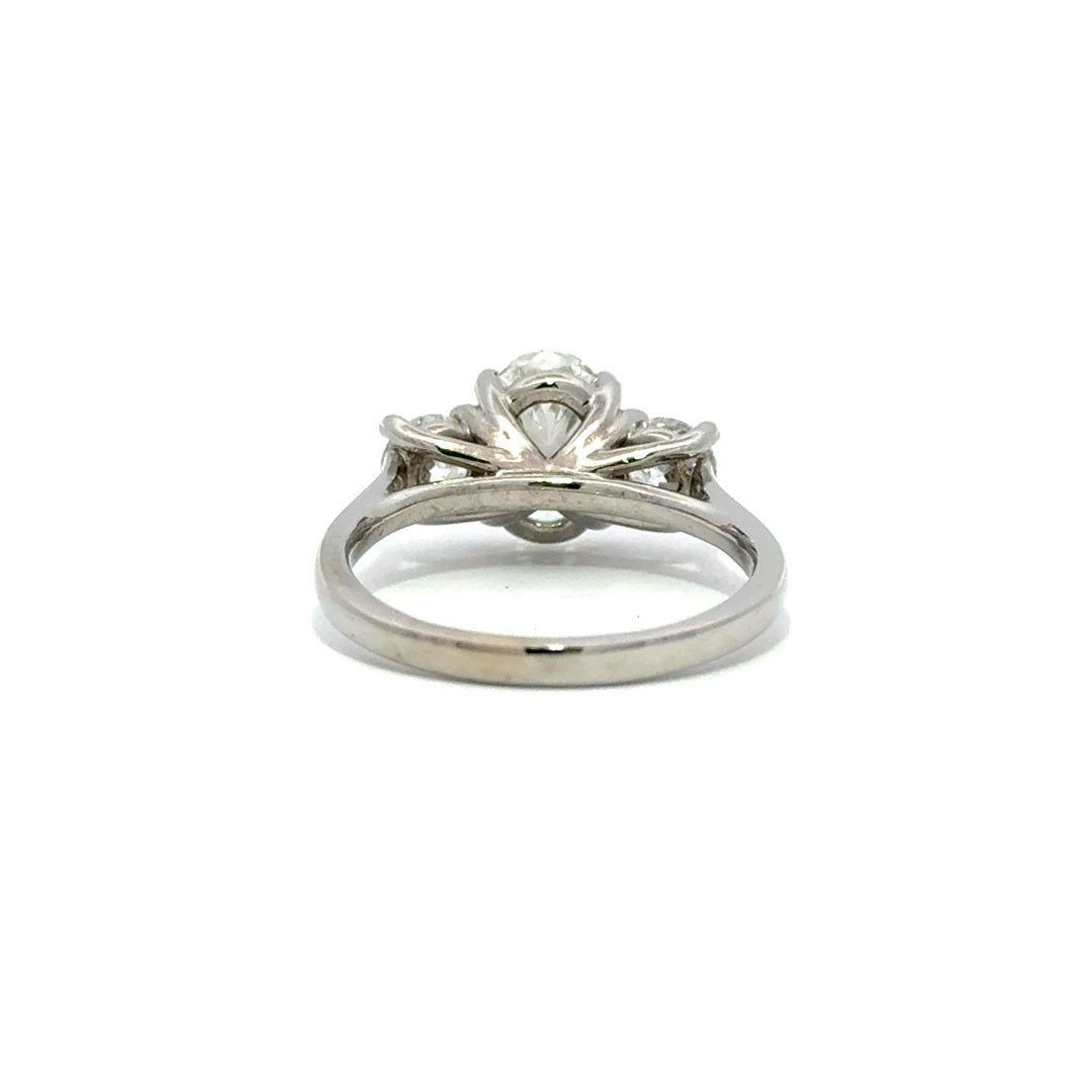 Silver three-stone engagement ring with pear-shaped center diamond and round side diamonds, on a white background.