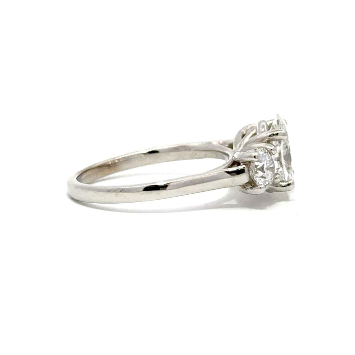 Silver three-stone engagement ring with pear-shaped center diamond and round side diamonds, on a white background.