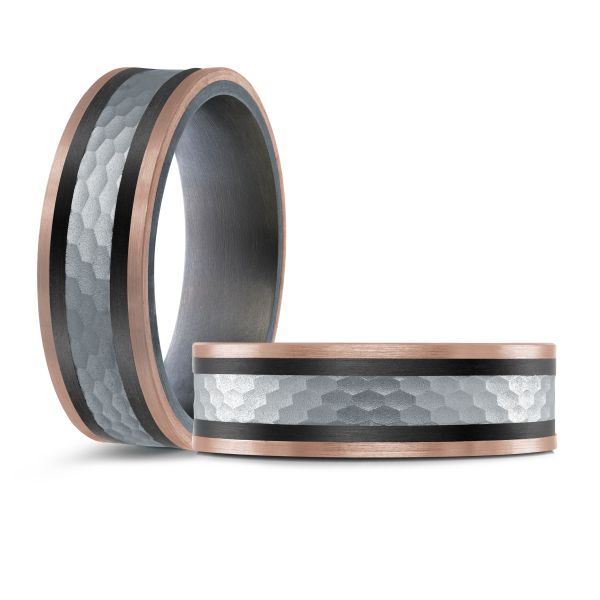 Black ceramic wedding band with a rose gold and hammered metal inlay on a white background