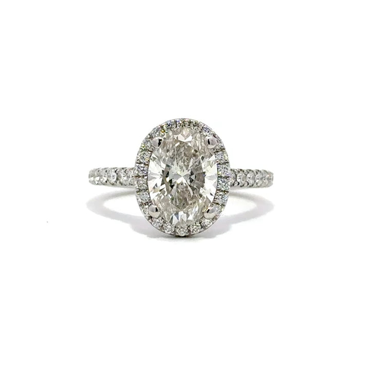 Silver ring with an oval-cut diamond center stone surrounded by a diamond halo and a diamond-studded band, on a white background.