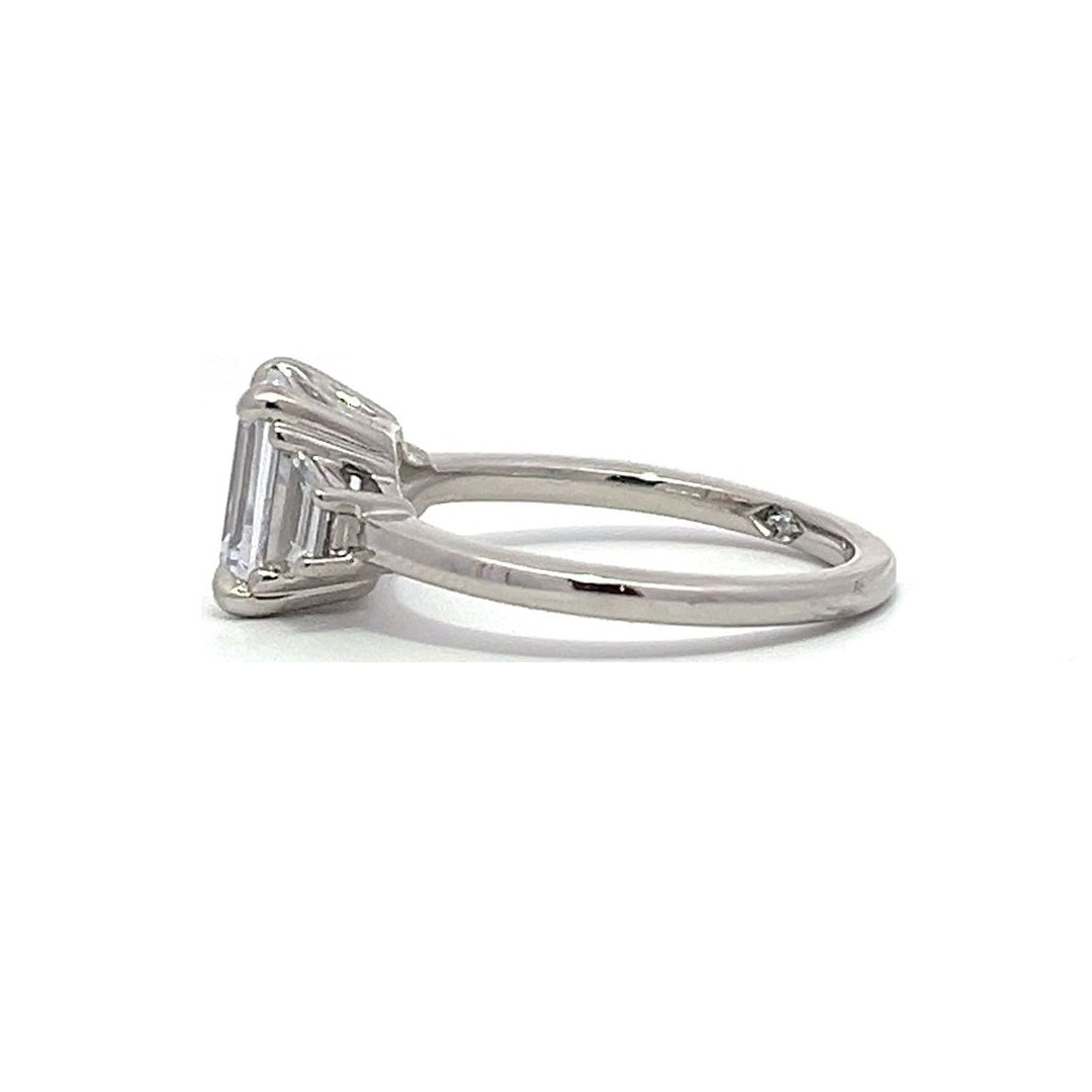  White gold three-stone diamond engagement ring with emerald-cut center stone and baguette side stones on a white background.