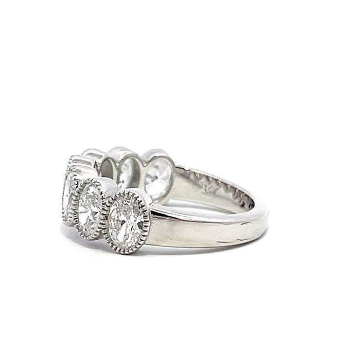 White gold eternity band with bezel-set oval diamonds on a white background.
