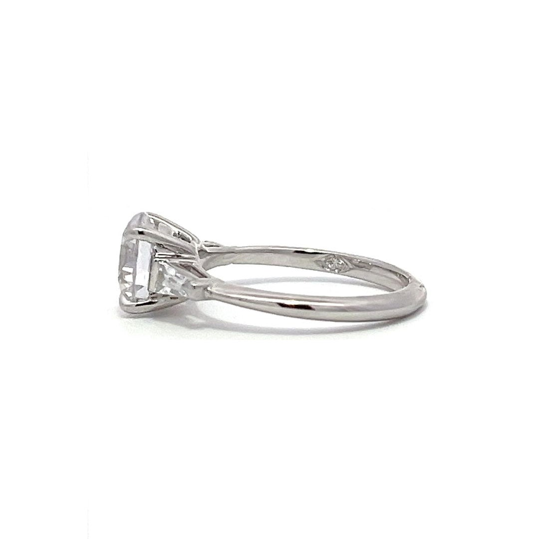  White gold three-stone diamond engagement ring with round-cut center stone and baguette side stones on a white background.