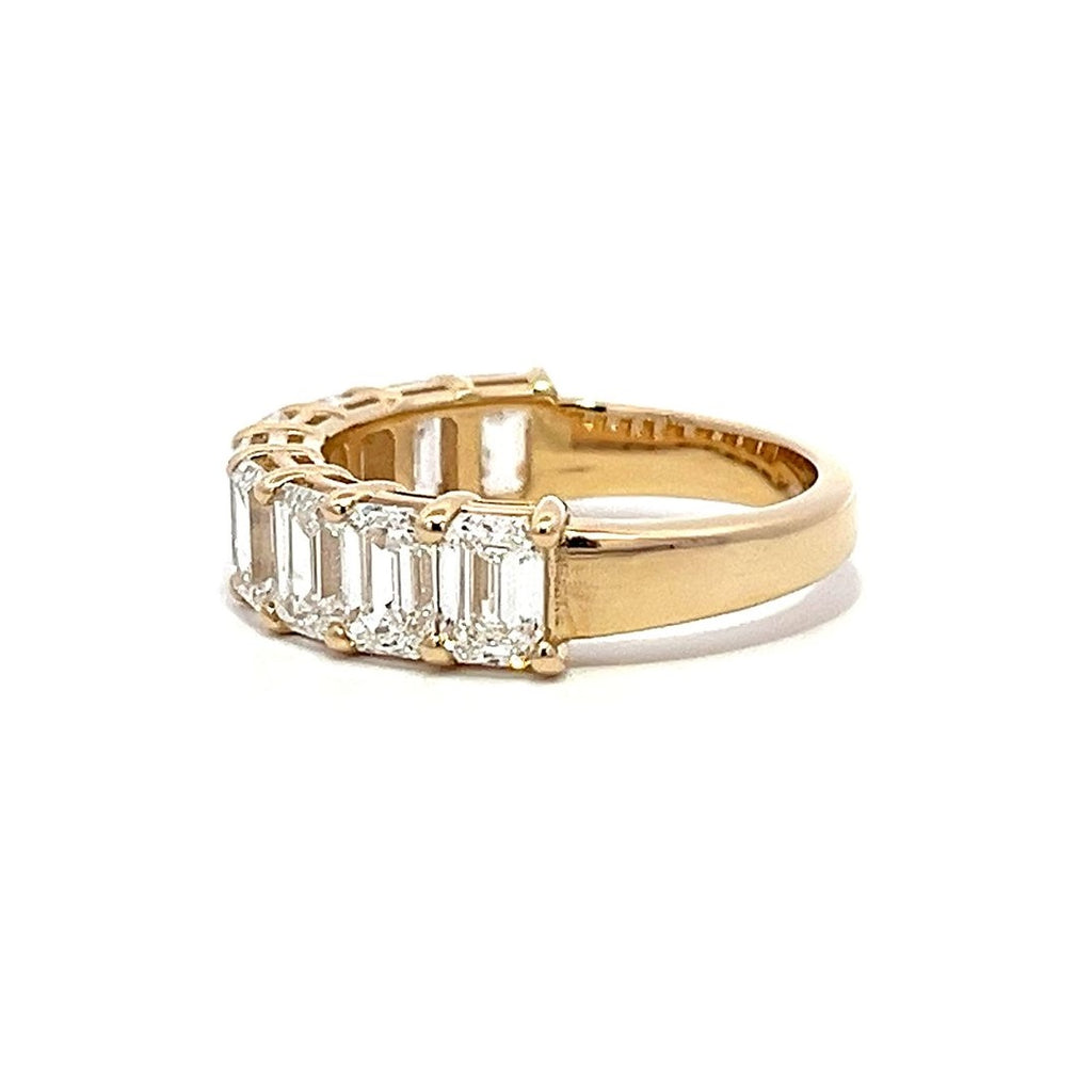 Yellow gold eternity band with emerald-cut diamonds on a white background.