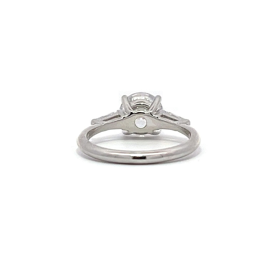  White gold three-stone diamond engagement ring with round-cut center stone and baguette side stones on a white background.