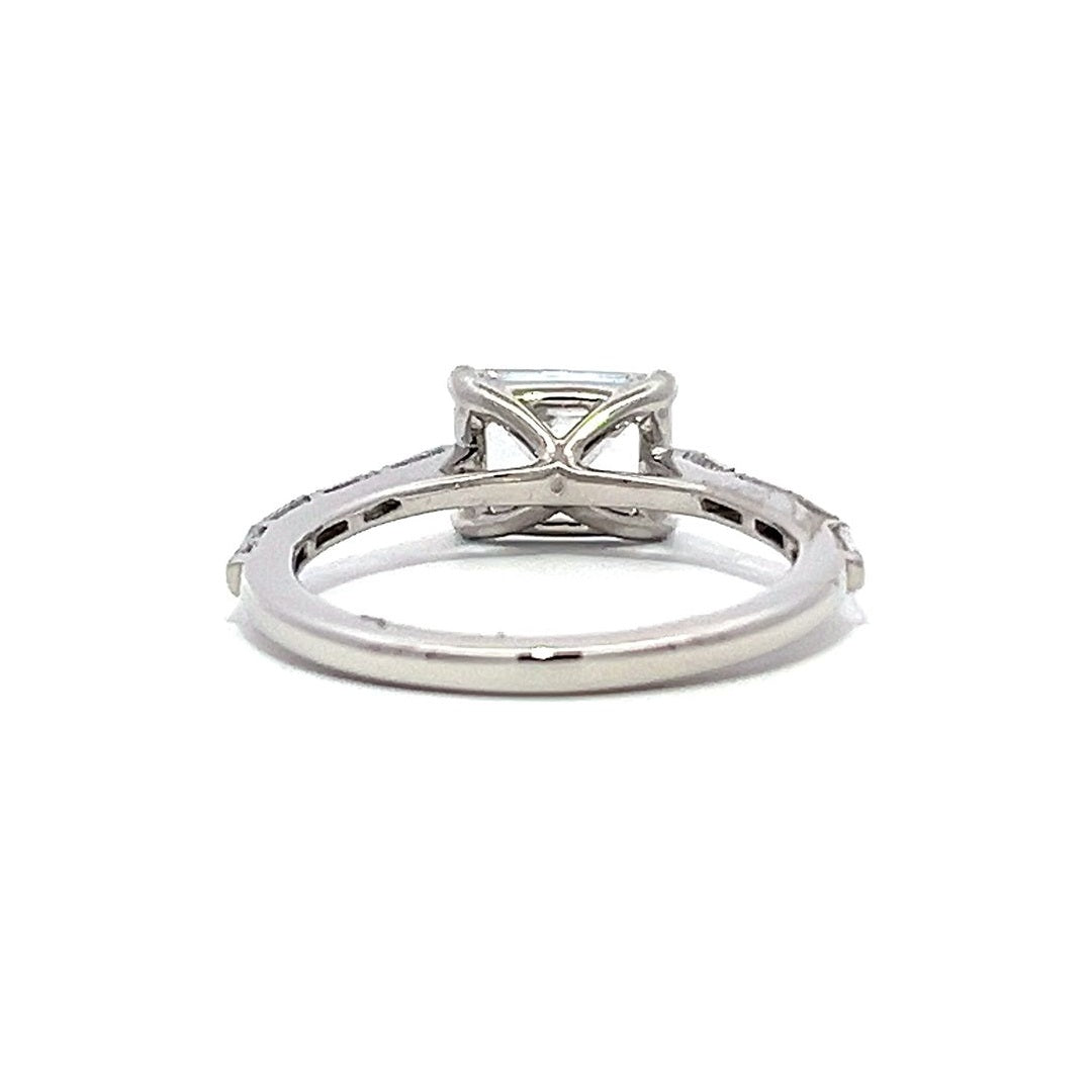 White gold emerald-cut diamond engagement ring with a diamond band on a white background.