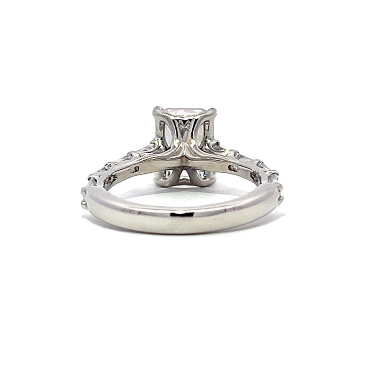 White gold emerald-cut diamond engagement ring with a diamond band on a white background.