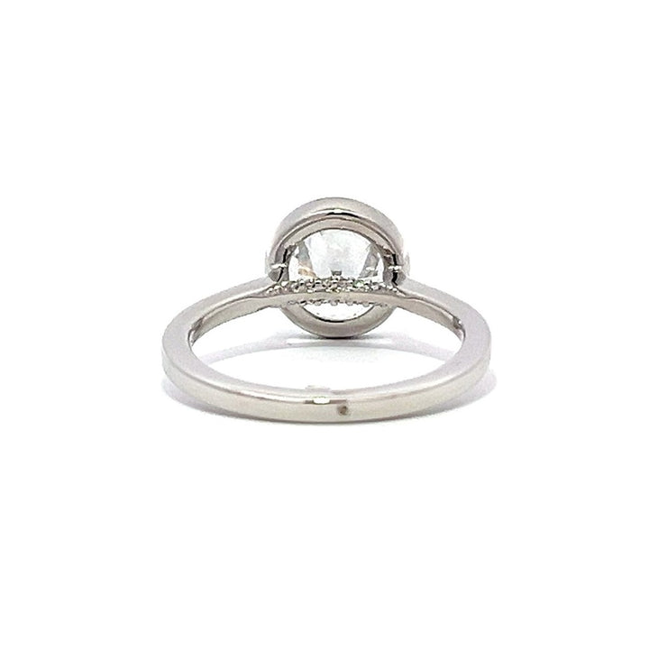 White gold bezel-set diamond engagement ring with a diamond band on a white background.