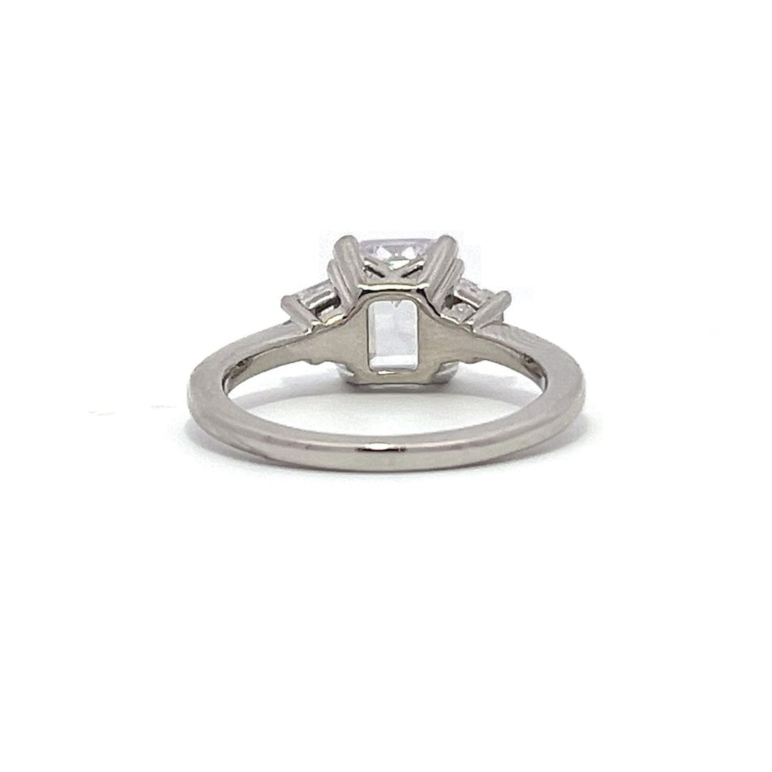  White gold three-stone diamond engagement ring with emerald-cut center stone and baguette side stones on a white background.