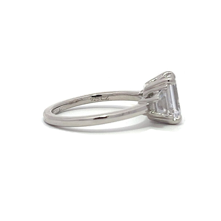  White gold three-stone diamond engagement ring with emerald-cut center stone and baguette side stones on a white background.