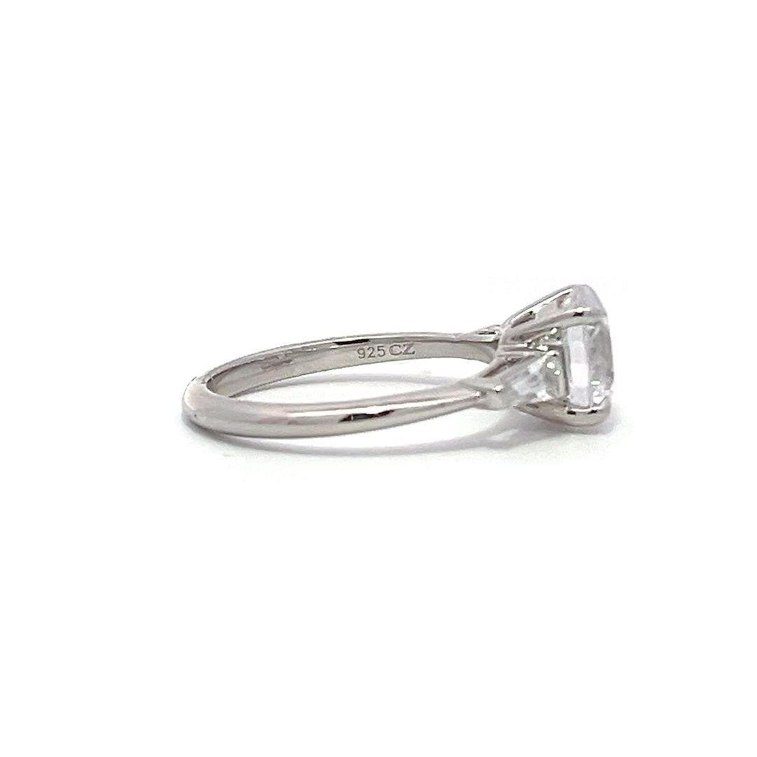  White gold three-stone diamond engagement ring with round-cut center stone and baguette side stones on a white background.