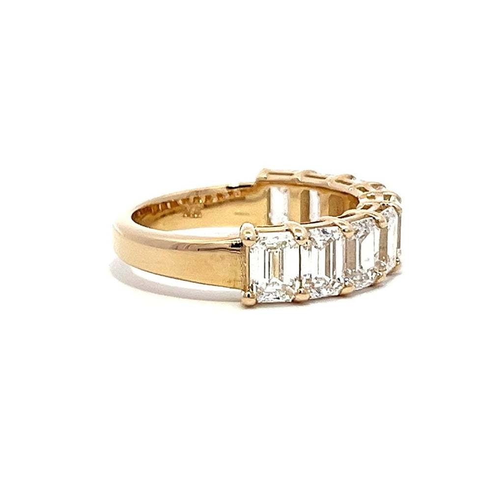 Yellow gold eternity band with emerald-cut diamonds on a white background.