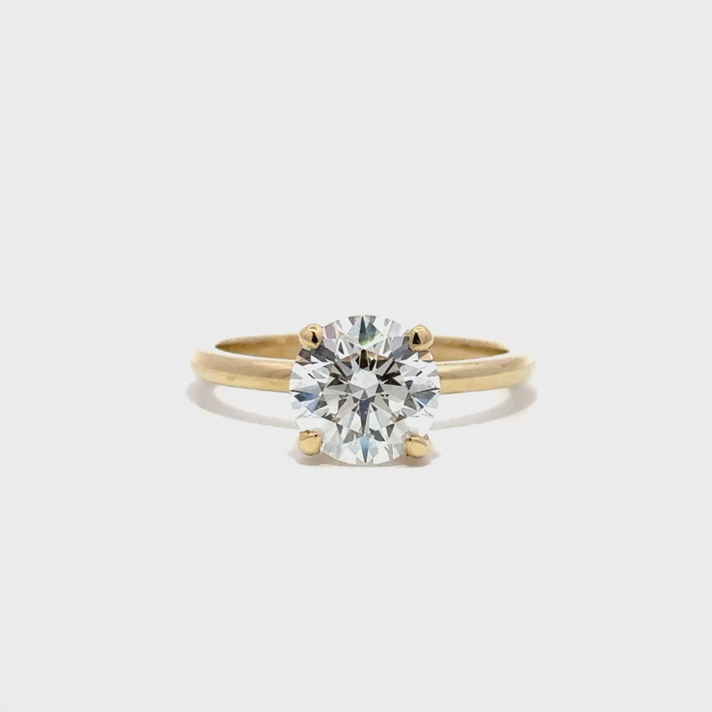 Yellow gold solitaire engagement ring with a round-cut diamond center stone on a white background.