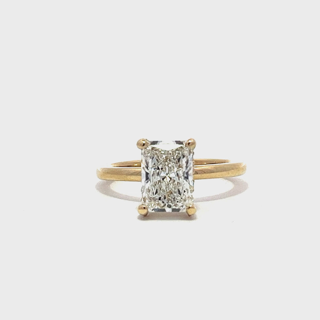 Yellow gold engagement ring with a radiant-cut diamond center stone on a white background.