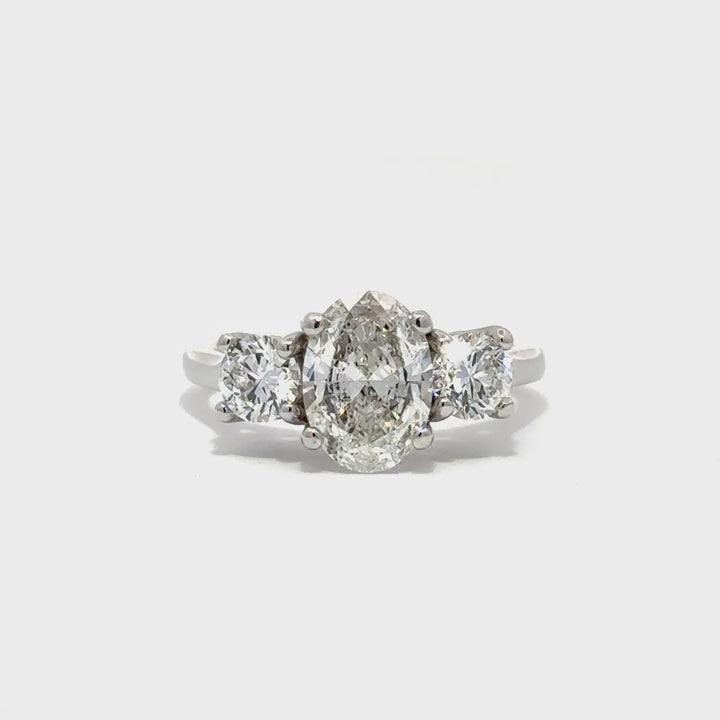 Silver three-stone engagement ring with pear-shaped center diamond and round side diamonds, on a white background.