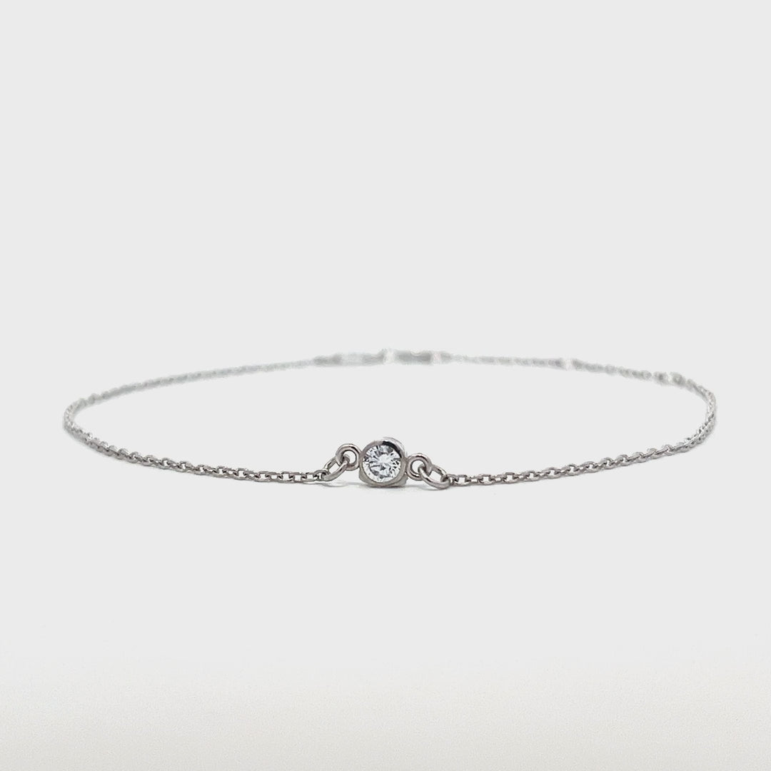 Silver bracelet with a single diamond pendant on a white background.