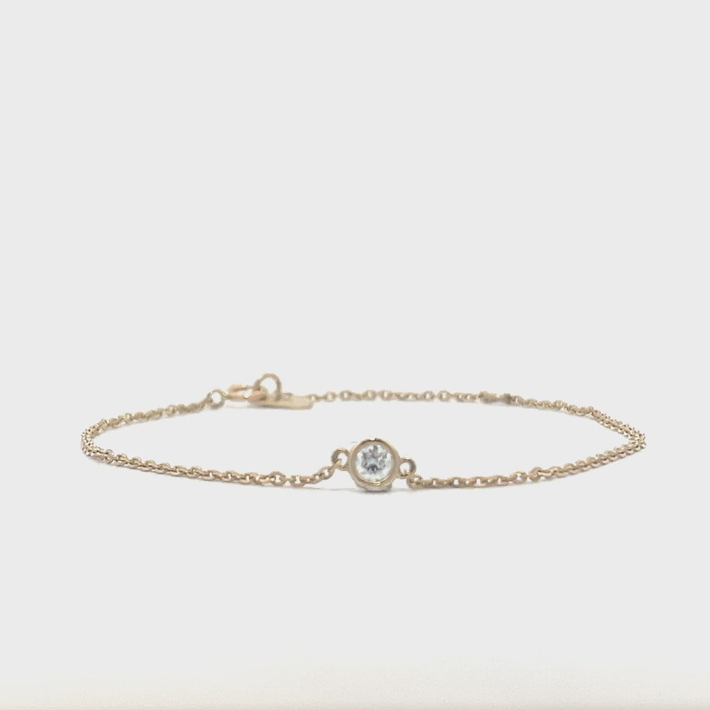 Yellow gold bracelet with a single diamond pendant in a bezel set on a white background.