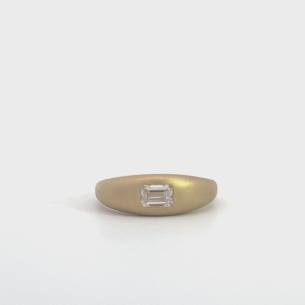 Yellow gold ring with an emerald-cut diamond set in a matte gold band, on a white background.