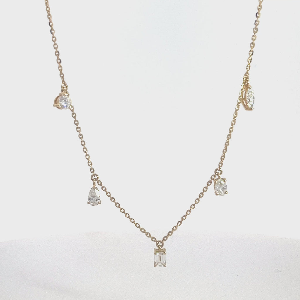 Yellow gold necklace with multiple diamond pendants, including round, pear, and emerald cuts, on a white background.