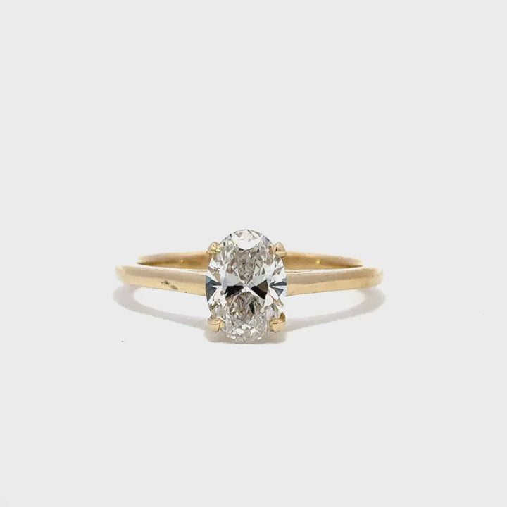 Yellow gold solitaire engagement ring with a oval cut diamond center stone on a white background.