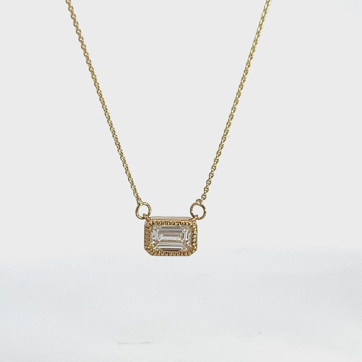 Yellow gold necklace with an emerald-cut diamond pendant on a white background.