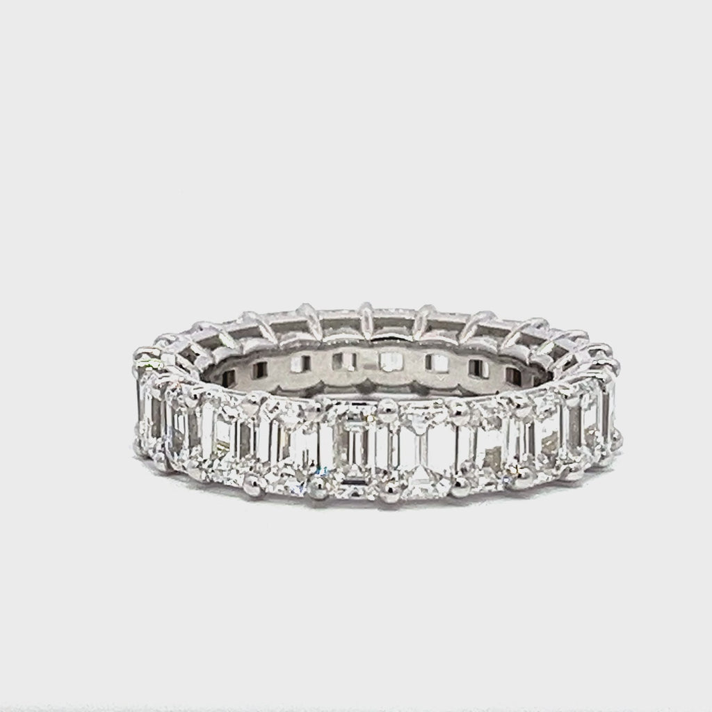 Silver eternity band with emerald-shaped diamonds on a white background.