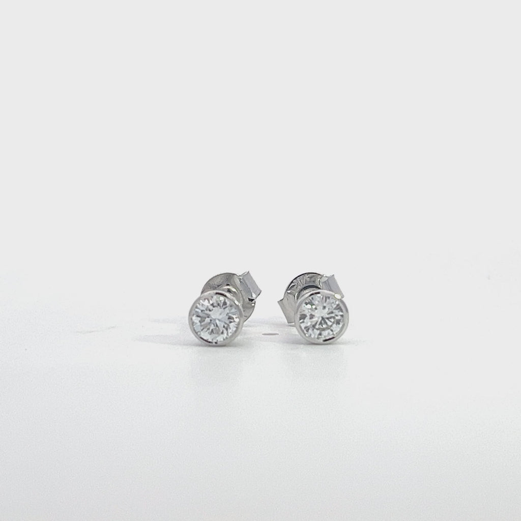 White gold stud earrings with round diamonds in  bezel setting on a white background.