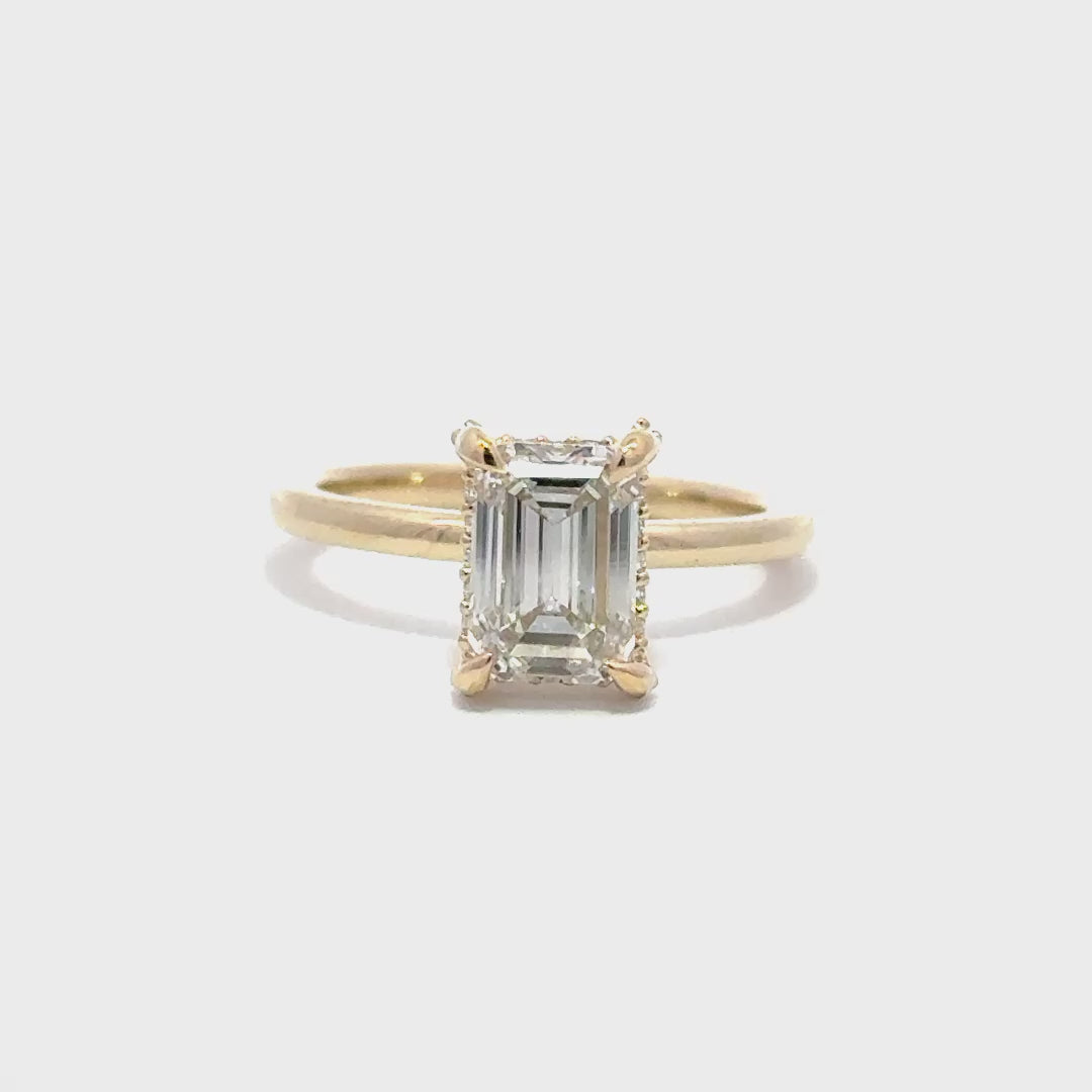 Yellow gold engagement ring with a center emerald cut diamond.