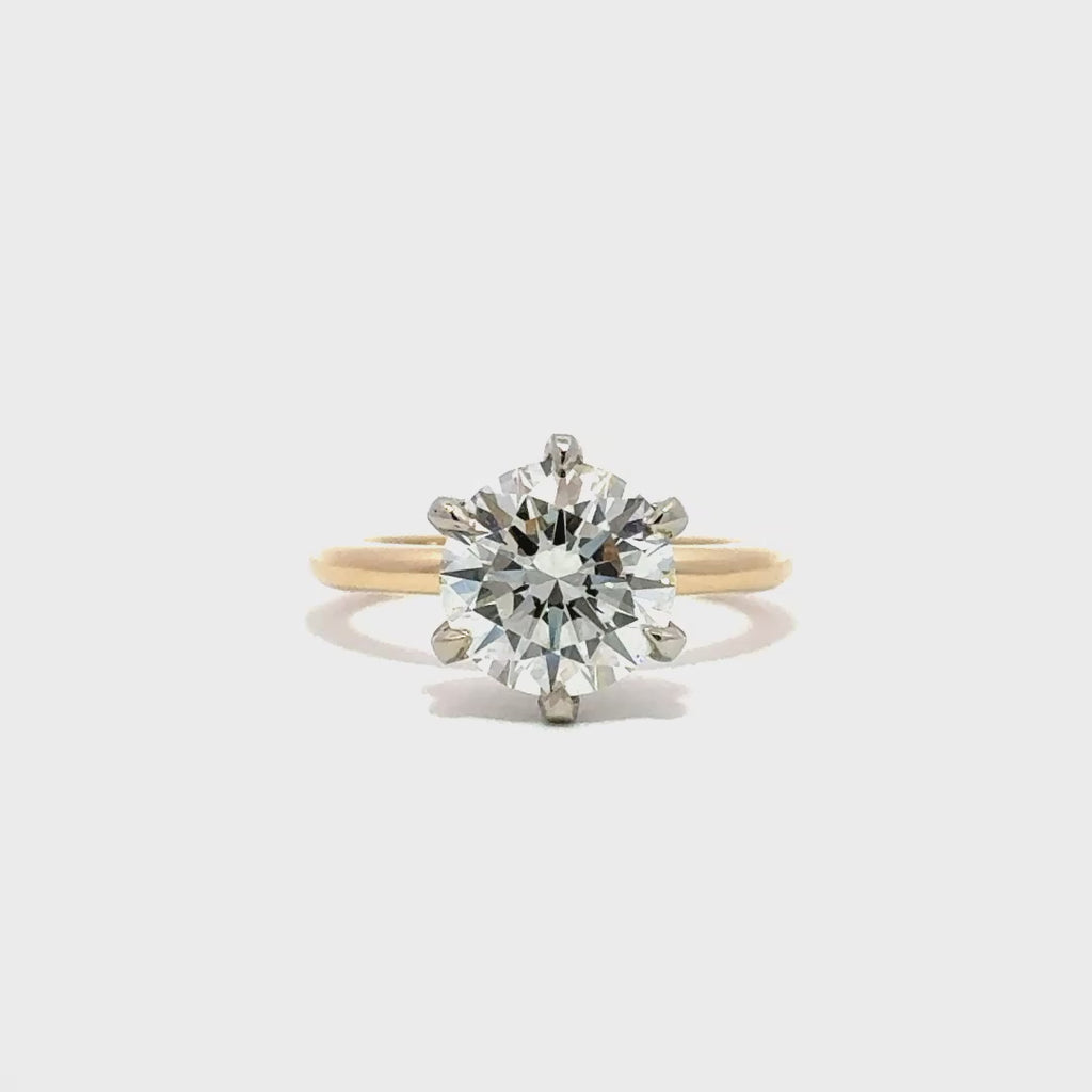 Yellow gold solitaire engagement ring with a round-cut diamond center stone and silver prong on a white background.