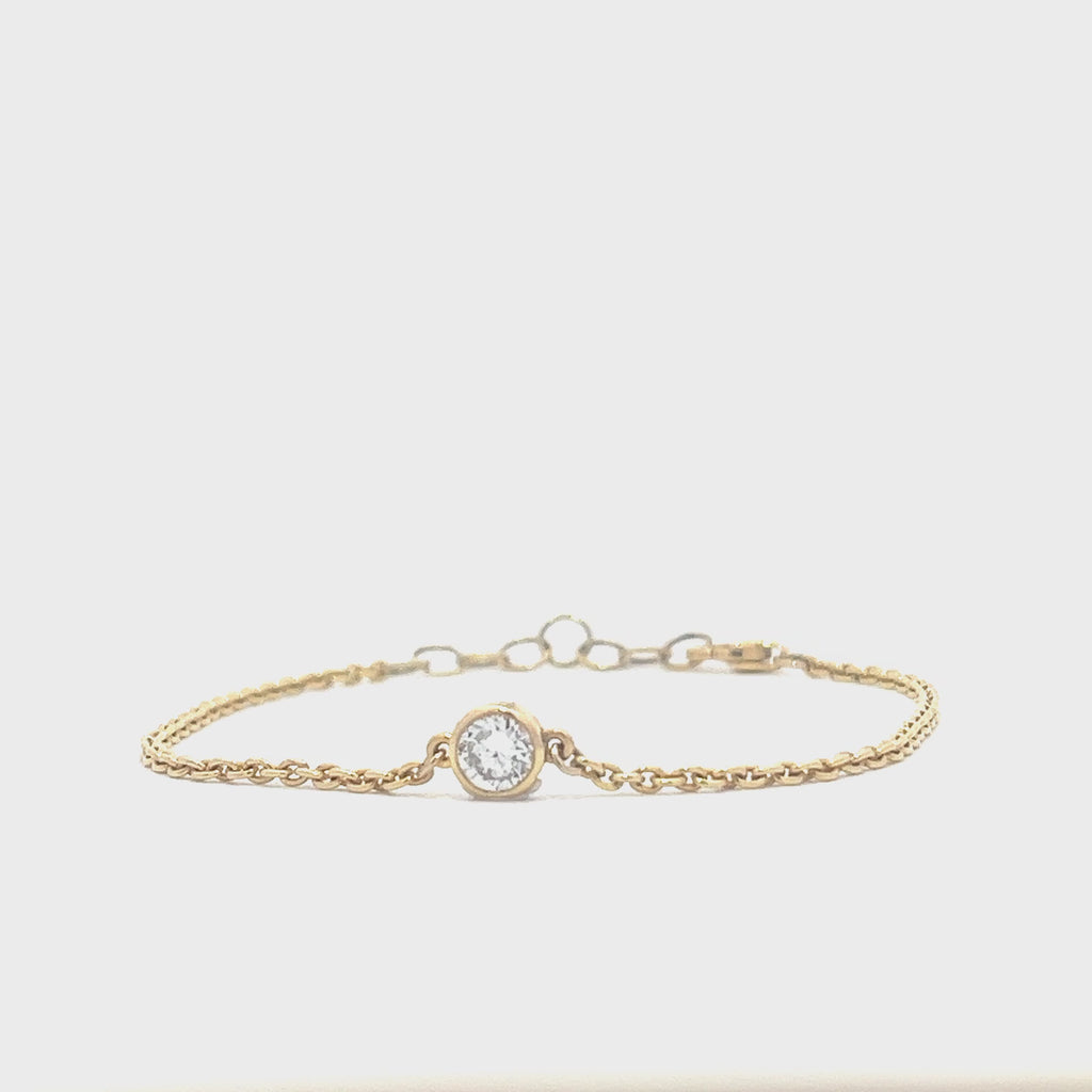 Yellow gold bracelet with a single diamond pendant in a bezel set on a white background.